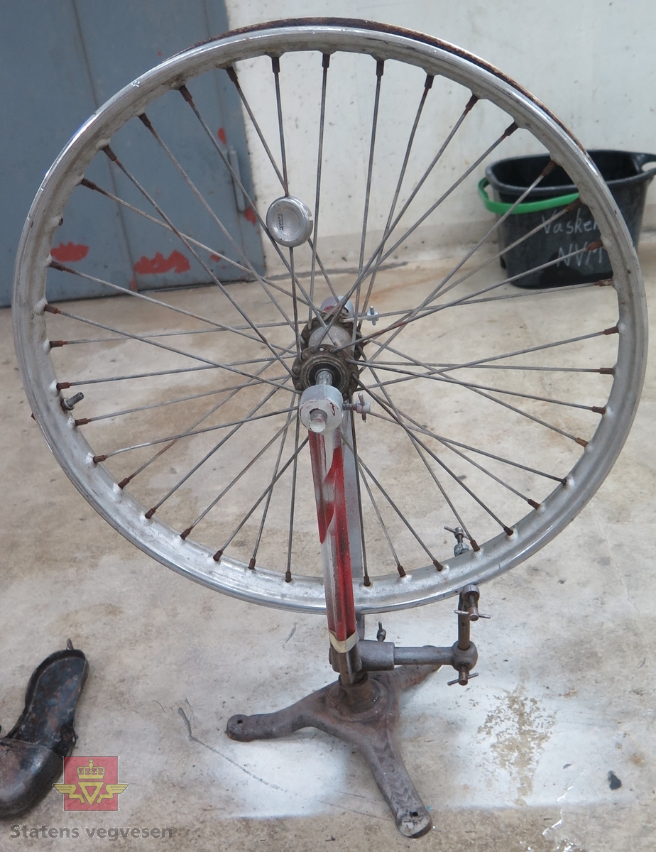 Stativ av metall, med et motorsykkelhjul festet til. Verktøy for stramming av eiker følger med. Ved å skru på eikene kan en rette opp skevheter i hjulet (felgen).
