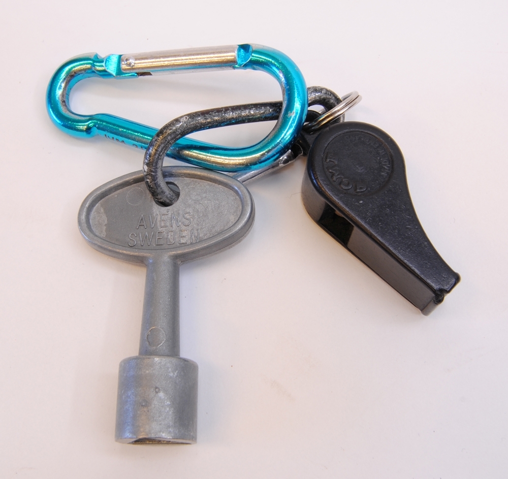 Godsvagnsnyckel. På ena sidan står det "AVÉNS SWEDEN" och på andra sidan "PG 312". Nyckeln har en invändig trekant.