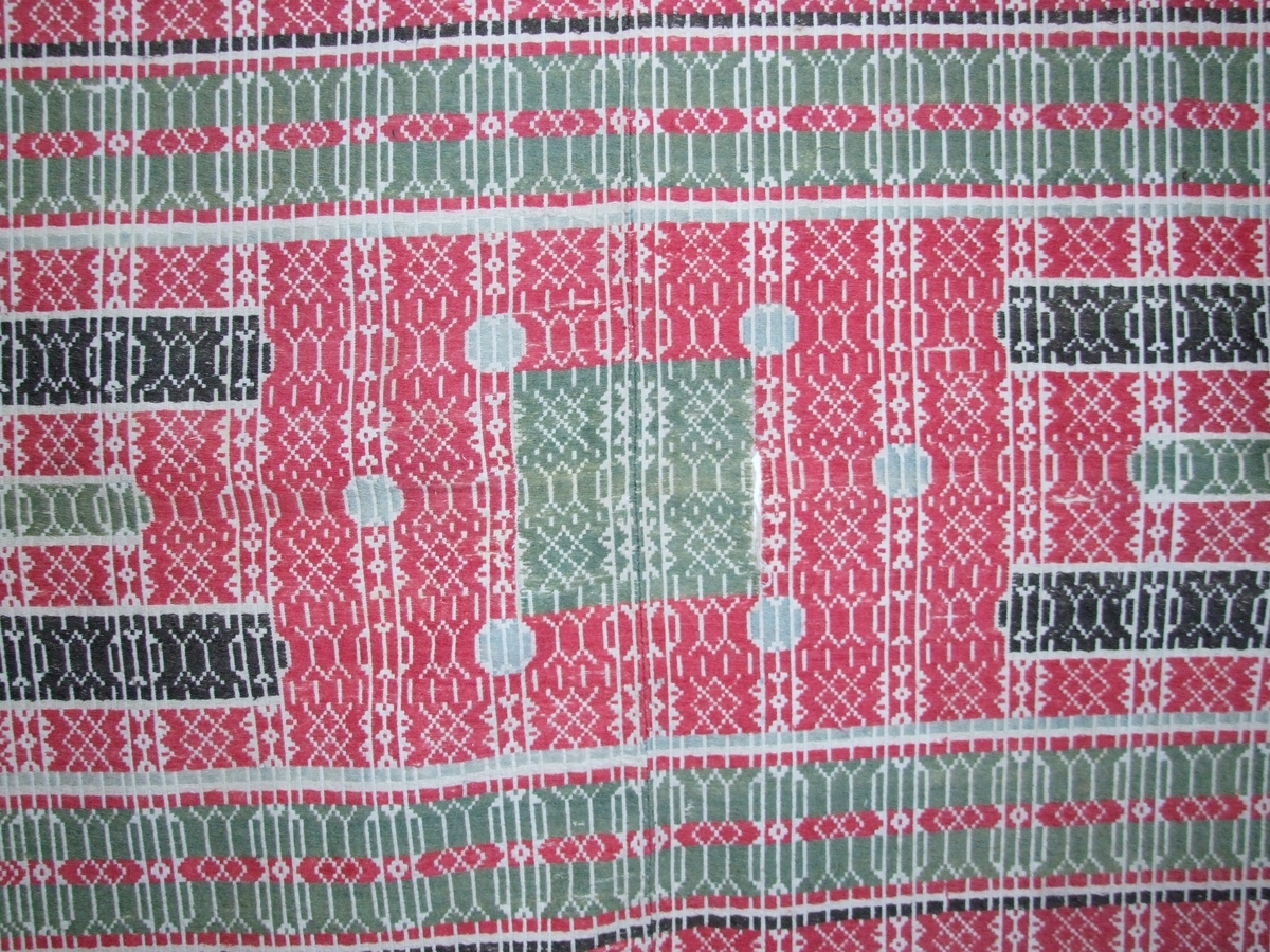 Smetta grøn frikant på raud (korsforma?) innramming midt på teppet. 