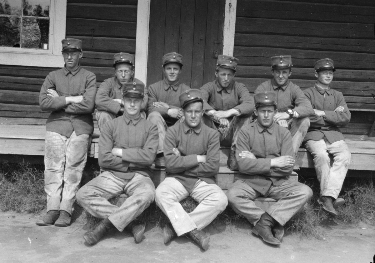 Ti soldater poserer på ei trapp utenfor en tømmerbygning.