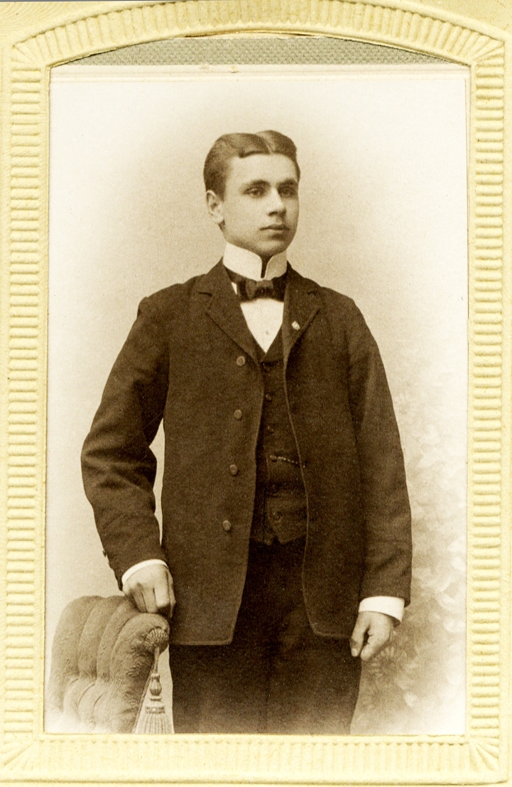 Foto av en ung man i kostym med väst, stärkkrage och fluga.
Knäbild, halvprofil. Ateljéfoto.