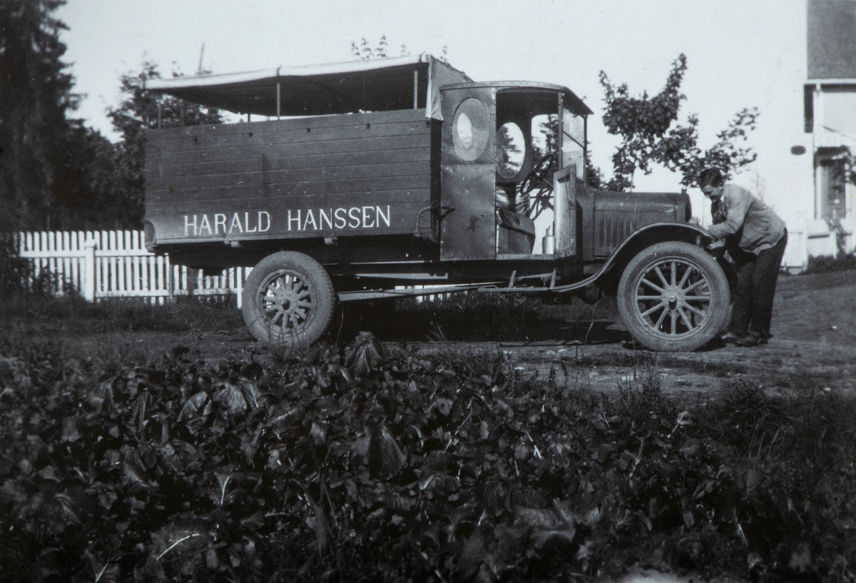 Lastebil, varebil. Lastebilen til Landhandler Harald Hansen, stående foran butikken. Mens Alf Oseth (f: 1908) prøver å svinge sveiva for å starte bilen. Rokosjøen, Løten.