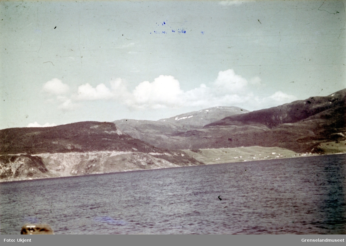 Ukjent sted langs kysten i Nord-Norge under andre verdenskrig.Nederst i venstre hjørne sees en uniformslue.