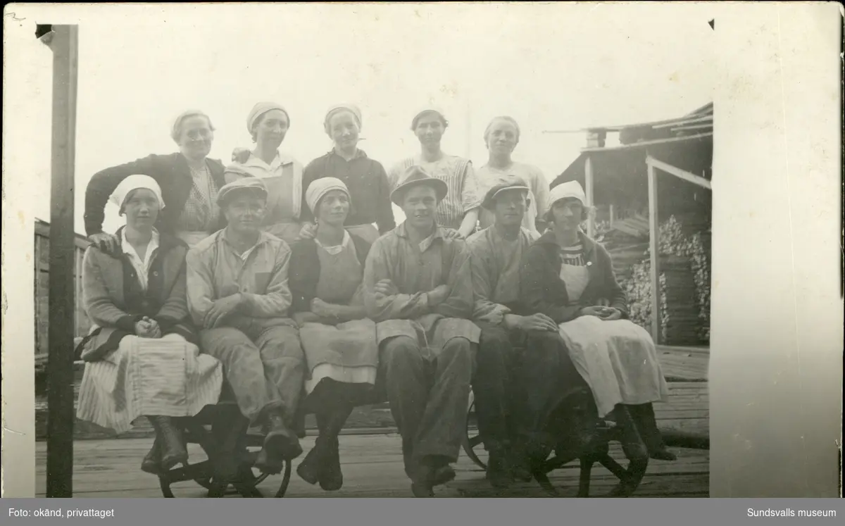 Vykort med motiv över fem stående och sex sittande personer i hamnmiljö. Enligt texten på baksidan: "Kolbackens lastarlag vid Svartvik 1922".