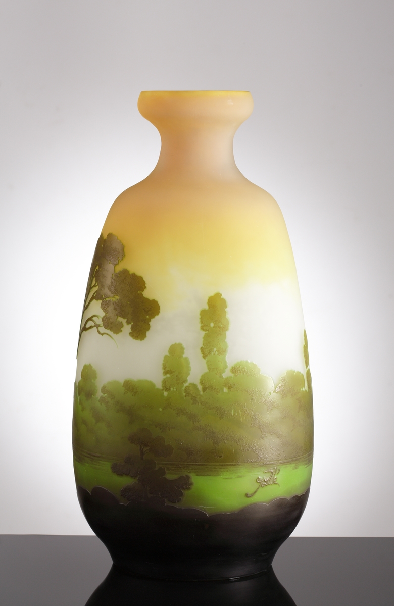 Opak vas som skiftar från orange, till gult, till vitt. Etsat överfång i gröna nyanser som avslutas i svart ner mot vasens botten. Motivet är ett sommarlandskap med en sjö och omgivande träd.
