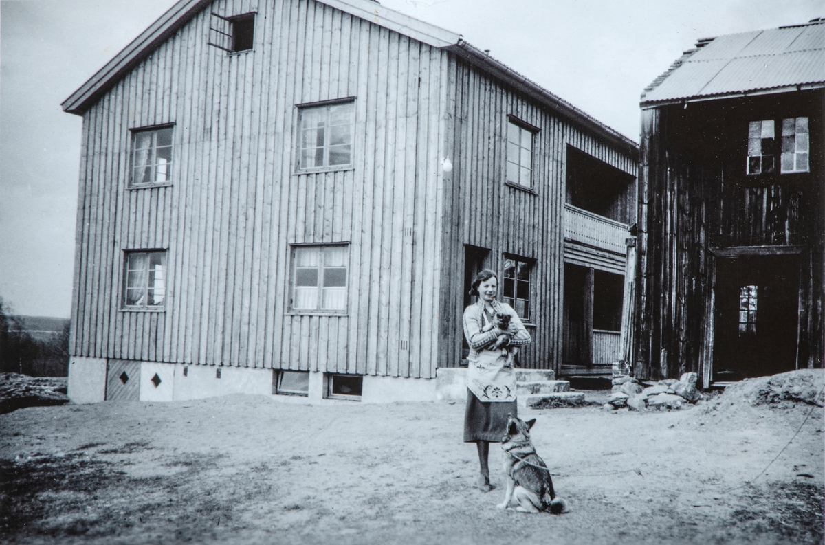 Harildstad Øvre, 333/1, Stange. I front Beate Nordstad (f.1901-d.1982) stående med en hundevalp i hendene, mens hunde mor sitter å følger med. Elghund.  Byggningen bak til venstre ble satt opp i 1939. Og byggningen til høyre ble revet senere samme år.