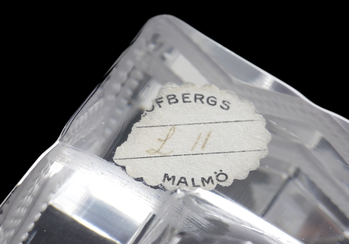 Askfat i klarglas med mattetsad dekor i sicksackmönster.
Etikett: Oval med vågig kant: "LÖFBERGS MALMÖ". I etikettens mitt handskrivet: "L 11"