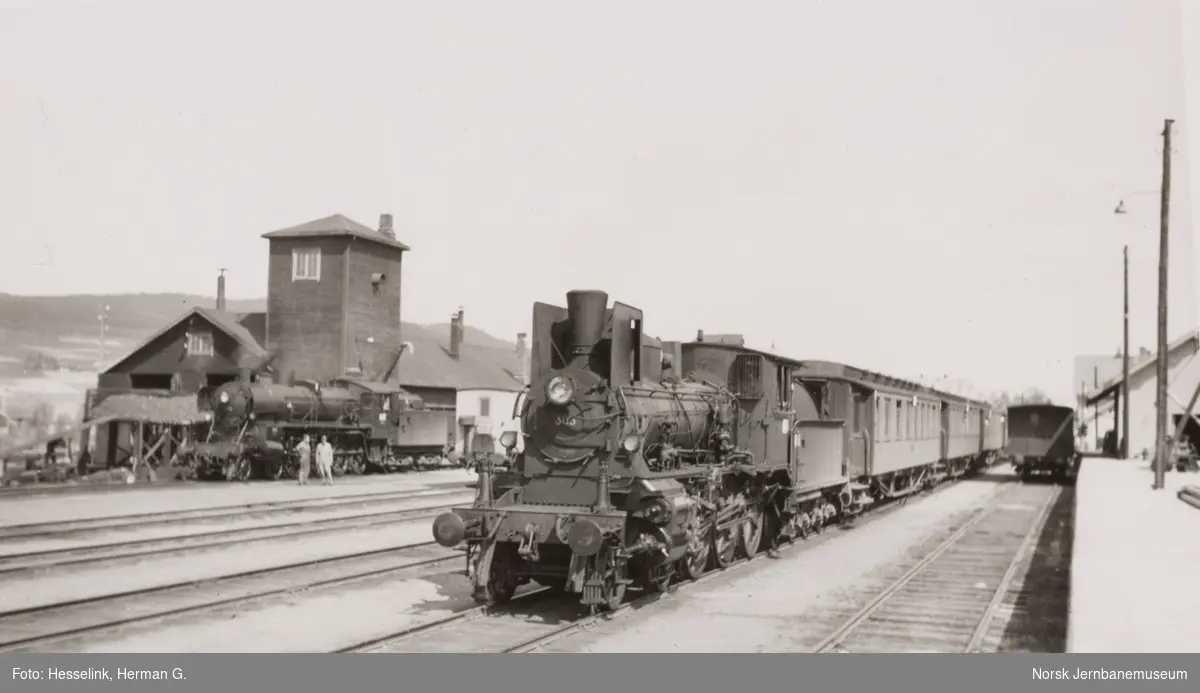 Damplokomotiv type 27a nr. 303 med dagtoget fra Trondheim til Oslo Ø over Røros, tog 302, på Tynset stasjon. Bak til venstre damplokomotiv type 26c