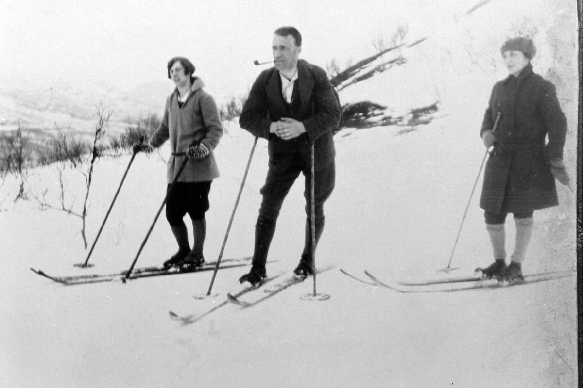 En mann og to kvinner på skitur tar en pust i bakken.