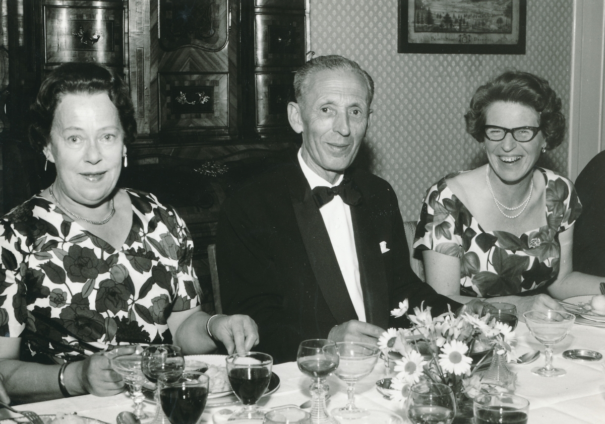 To kvinner og en mann i festantrekk ved festbord.