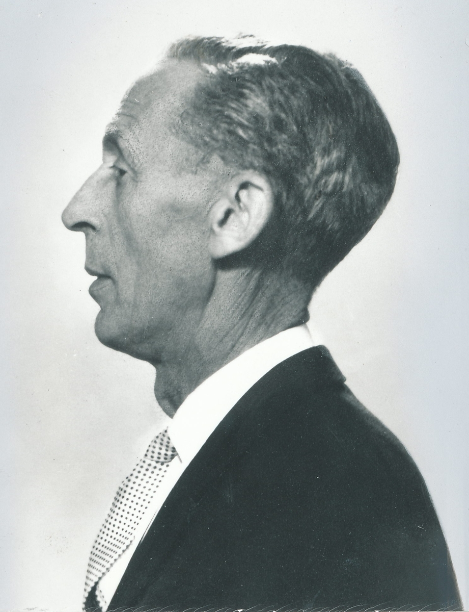 Portrett av mann i 50-årsalderen i profil. Iført dressjakke, skjorte og slips.