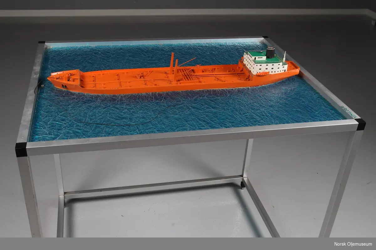 Modell av tankskip, såkalt bøyelaster - bygget i plast og montert på "sjø" av ruglet glassplate.