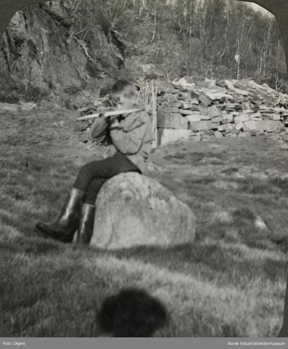 Olav O. Vågen sitter på en stein foran Dalstøyl. Olav er iført gummistøvler og holder antagelig et leketøy. Stølen ble brukt som en høybu