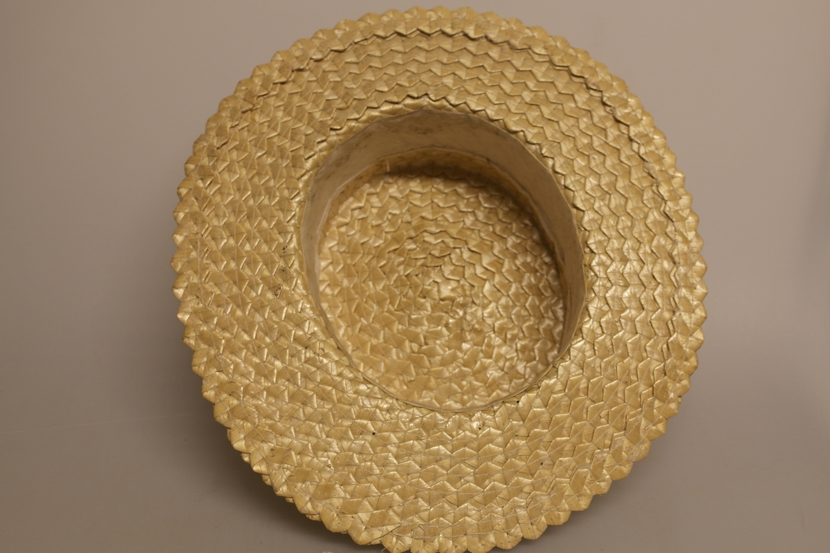 Naturfarget, oval stråhatt med flat pull. Hatten er sydd av flettede bånd av halm og har svart ripsbånd med sløyfe, samt hvit svetterem.