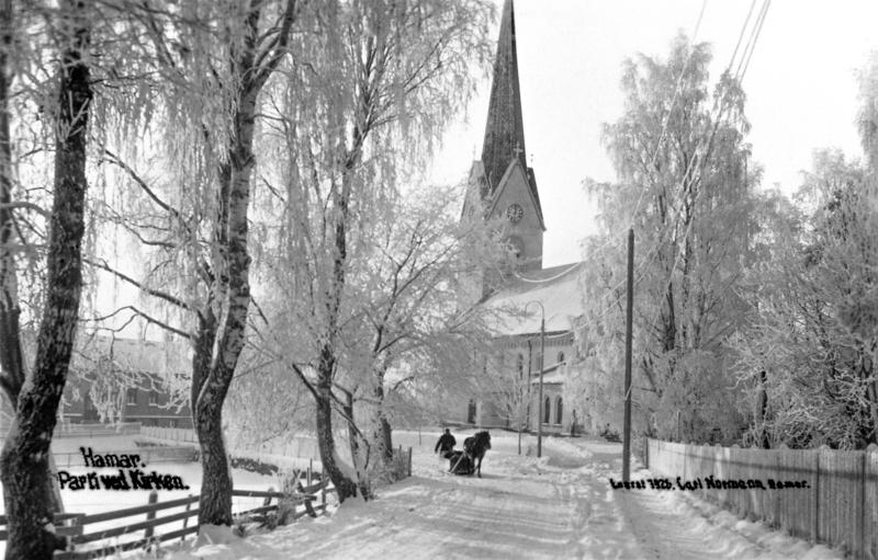 Svart-hvitt foto av rimete bjørketrær som leder ned mot Hamar Domkirke, og en hest med slede rett foran kirken. (Foto/Photo)