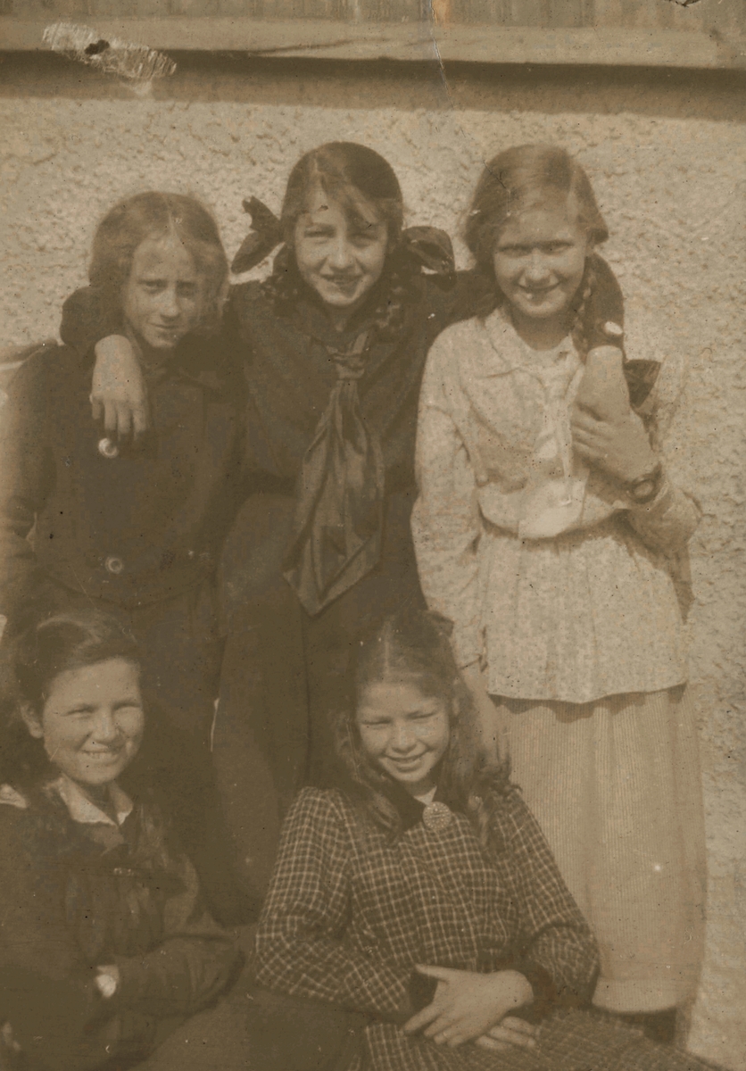 Portrettfotografi av fem unge jenter i penklær utenfor et hus.