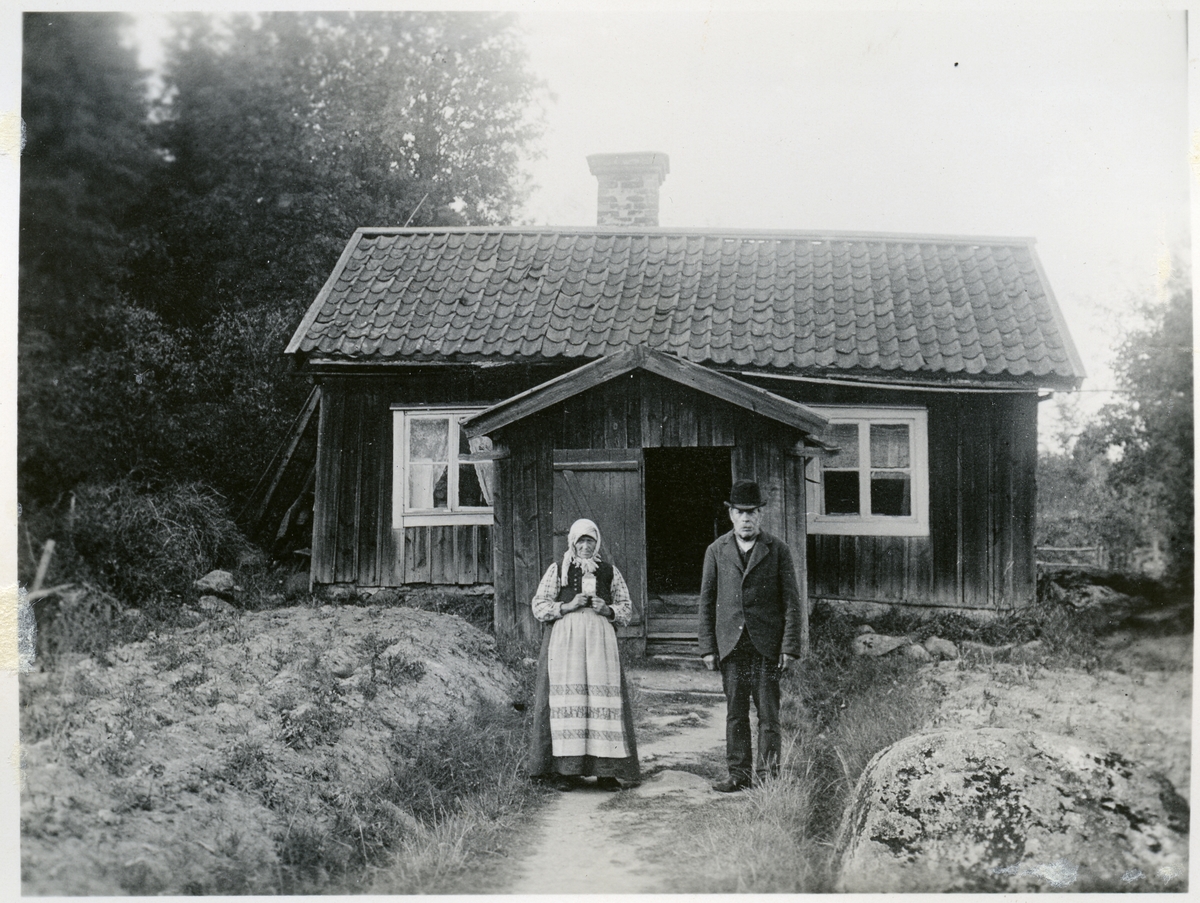 Skultuna sn, Västerås, Björneborg.
Skomakare Arrenius. Man och kvinna stående utanför bostaden. C:a 1900-1910.