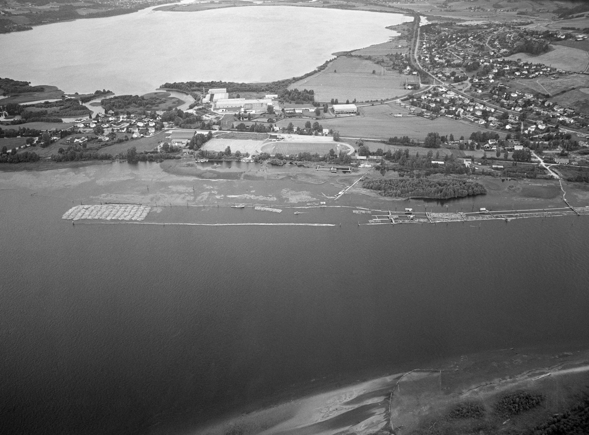 Flyfotografi fra Fetsund, som var kommunesenter i Fet kommune. Dette bildet ble tatt i 1985, fra en posisjon på den sørøstre sida av Glomma, med kameraet vendt nordvestover. I forgrunnen, på den nedre delen av bildeflata, ser vi Glomma, som her er i ferd med å renne inn i innsjøem Øyeren. Langs den vestre elvebredden ser vi den nedre delen av lenseanlegget. 1985 var den siste sesongen det ble «soppet» (buntet) tømmer for buksering sørover mot Nedre Glomma og Borregaard fabrikker i Sarpsborg. En del «sopper» lå klare for buksering gjennom deltaområdet. Vannspeilet i bakgrunnen er Svellet. Til høyre i bildet ser vi jernbanetraséen - Kongsvingerbanen - og boligfeltet Nedrum.