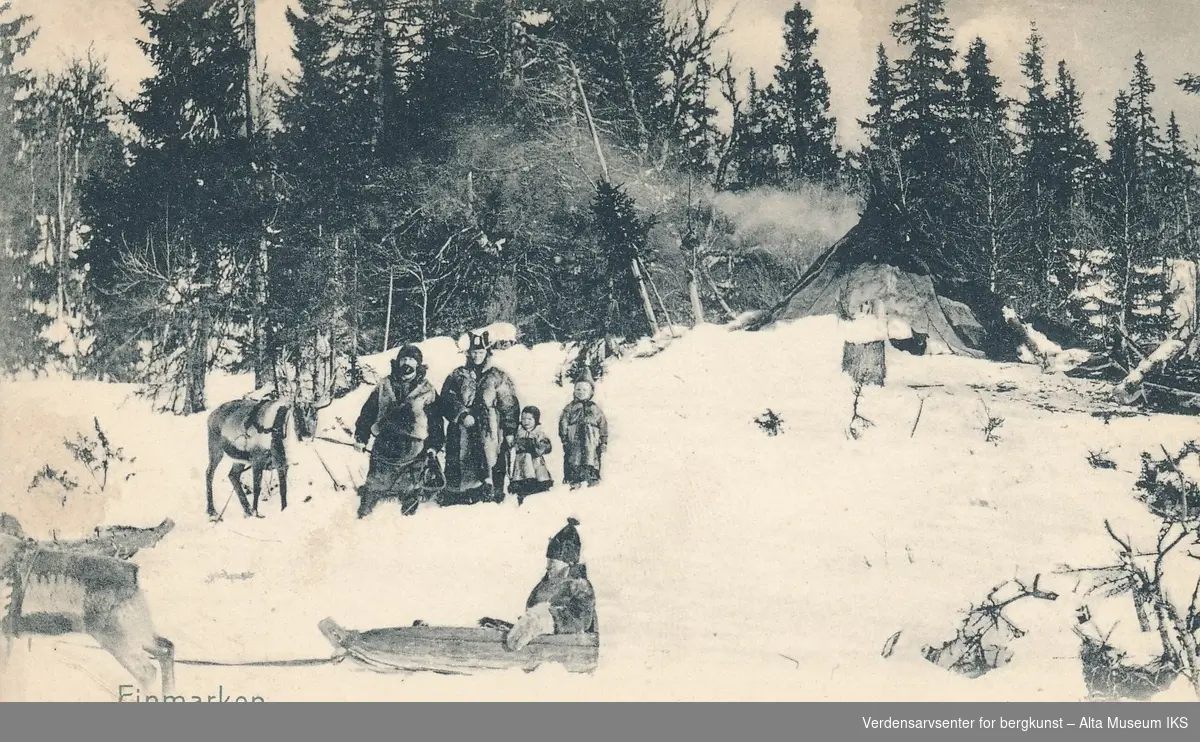 Landskapsbilde av en samisk familie foran en lavvo med bålrøyk  fra toppen. Familien består av mann, kone og to barn. Mannen holder et reinsdyr i bånd. En femte person blir trekt forbi i en pulk av en rein.
