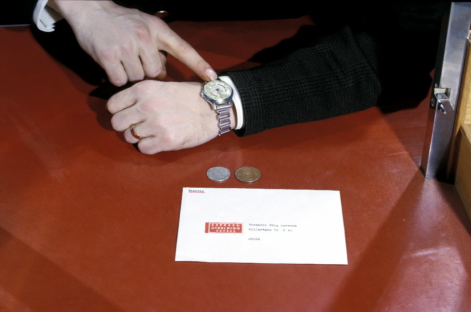 Seriebild H 3. Ett expressbrev lämnas in i kassa på potkontoret
Stockholm 40. Det adresserade kuvertet är försett med expressetikett.
Kunden visar med fing-ret på armbandsuret och antyder därmed att det
är brådskande.
