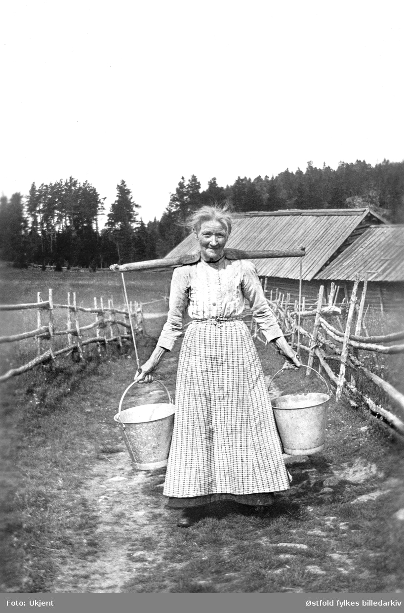 NIna Sørensen bærer vann, ca. 1920-1930. Opplysning 1996 fra barnebarnet til avbildete, kvinna heter Nina Sørensen, fra Rokke i Berg sogn.
Tidligere opplyst til å være Mina Hansen, Ulveholtet under Bunes,