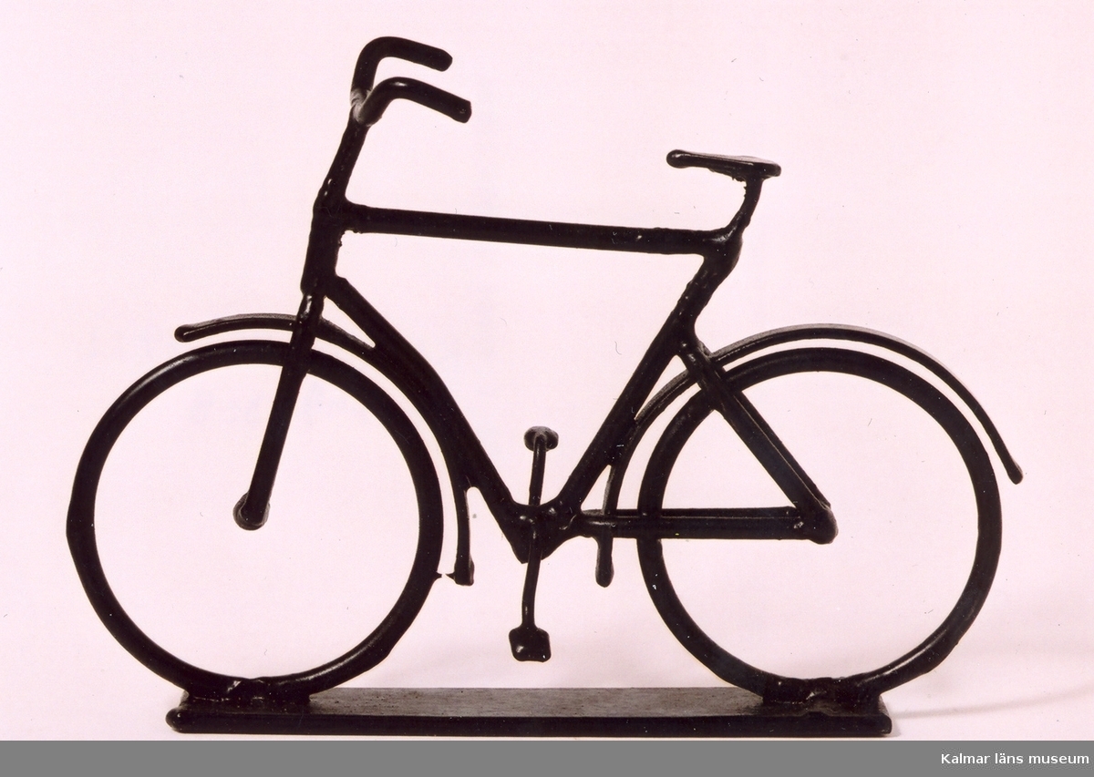 KLM 39586:49:1-2 Cykel med upphängningsanordning i form av en ram för att hängas på väggen, av metalltråd, svartmålad. Cykeln monterad på en metallplatta. Tillverkad i konstsmide, svetsad. Herrcykel med vanligt styre. Cykeln är inte monterad i den medföljande ramen. Prydnadsföremål. Tillverkad av Yngve Axtelius som var verksam som trådslöjdare.