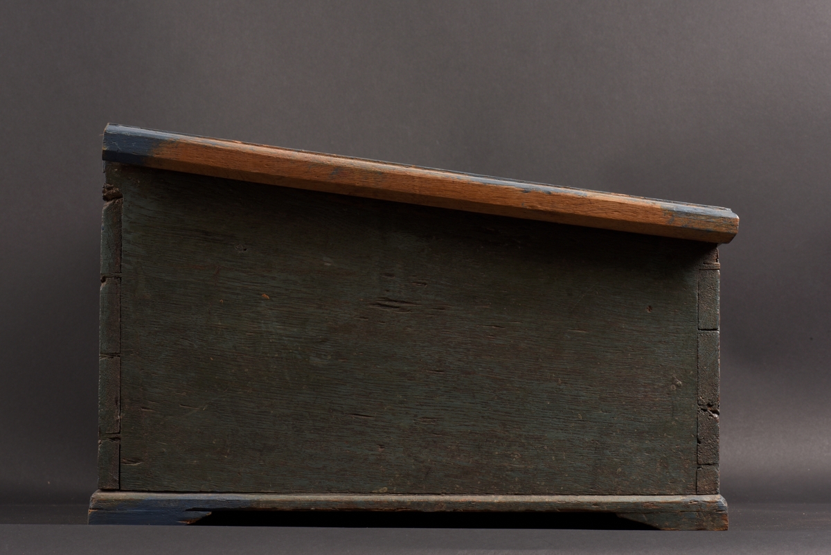 Rektangulärt skrin med lutande pulpetlock tillverkat av ek. Skrinet är blåmålat, men har ursprungligen varit grönt. På kanterna senare bättringsmålat med blå färg. På locket en målad rokokokartusch, i den ditmålade initialer, MJD, samt årtalet 1806. Inuti ett fack, läddika, utan lock.
Nyckel och låsbeslag saknas.