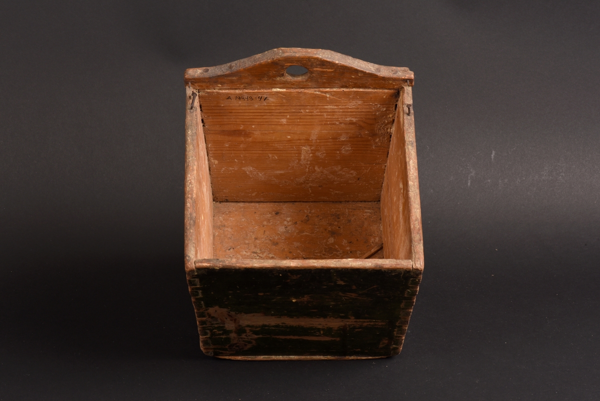 Kvadratisk låda av trä, troligen en låda för mjöl. Målad i mörkgrön färg på utsidan. Bakstycket är något högre och har en svängd kant, där ett hål för upphängning finns. Lock saknas.