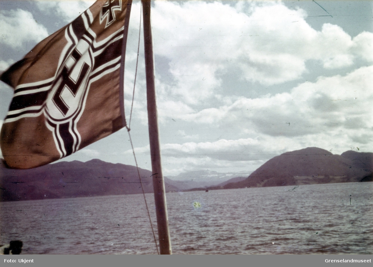 Orlogsflagg, flagg med hakekors akterut på et skip i Saltdalsfjorden mot Rognan. 