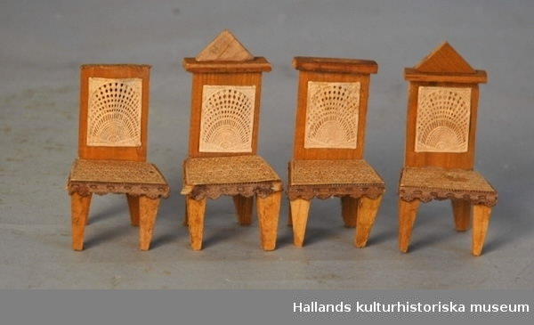 Dockmöbler - stolar, av gulbrunt trä, formad sits, rektangulärt ryggstöd. Påklistrat beige spetsmönstrat papper. Tre stolar har en rektangulär avslutning på ryggstödet, en saknar detta.