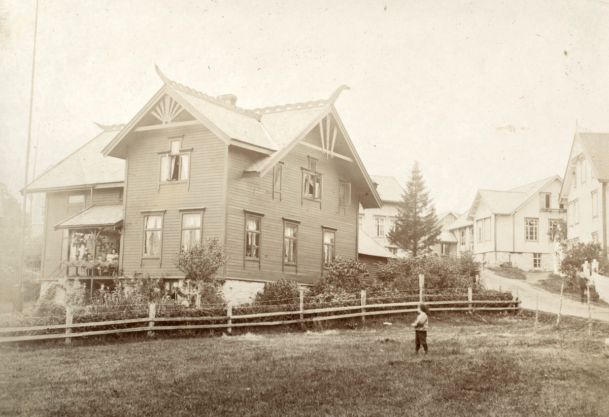 Prospektfotografi av et hus i dragestil i et boligområde. En gutt står på marka foran.