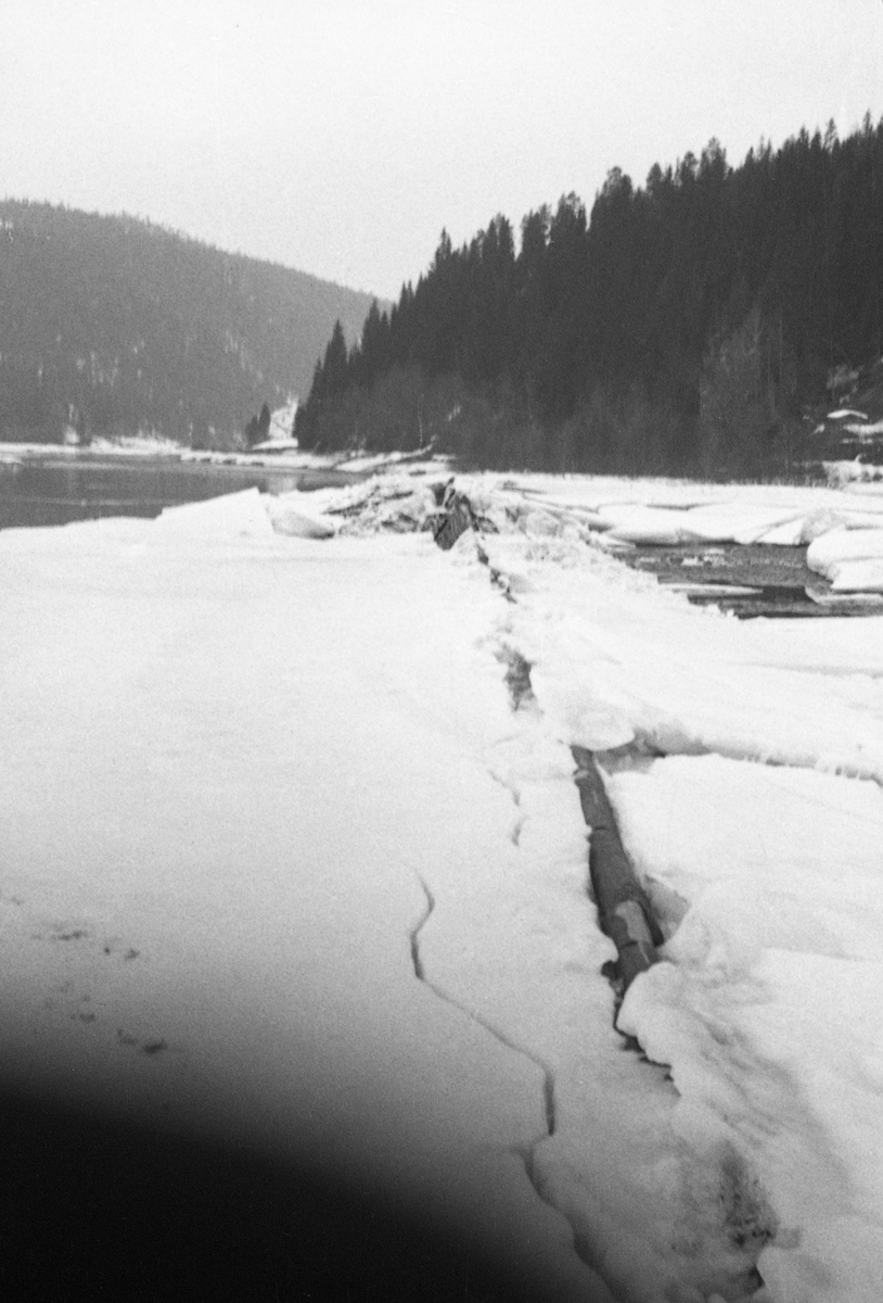 Fra Melvolldammen i den nedre delen av Renaelva i Åmot i Hedmark, fotografert på seinvinteren 1941. Bildet er tatt i medstrøms retning langsetter en såkalt skådam, en skjerm som skulle frastøte tømmeret fra elvebredden og få det til å flyte mot en djupere og mer hurtigstrømmende del av elveløpet. Da dette fotografiet ble tatt var dammen dekt av snø og is, som hadde sprukket der hvor konstruksjonen - antakelig en lav tømmervegg montert på bukker med forankring i en bakenforliggende steinvoll - møtte elva.