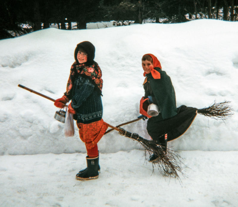 To jenter utkledd som gamle kjerringer med skaut på hodet står ved en snøkant med hver sin sopelime mellom bena, klare til å fly av gårde som påskehekser.