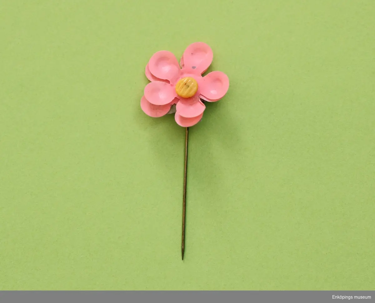 Majblomma från år 1924.
Blomman är gjord av rosa celluloid och har fem blad i dubbla lager, totalt 10 blad och en gul mittknapp, även denna gjord av celluloid. 
Under kronbladen finns spetsiga, gröna foderblad. Det som håller blomman samman är en nål av mässing.