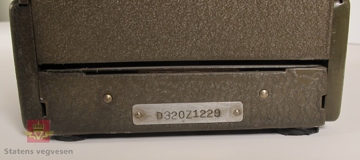 Protektograf i metall med påskriften PROTECTOGRAPH INTERNATIONAL Model 32 THE TODD COMPANY ROCHESTER.N.Y.,U.S.A. Har serienummer D320Z1229 montert på en metallplate bak på maskinen. Den har to sveivehåndtak, og betjeningspanel for innstilling av siffer. Den er i fungerende tilstand og stempler H.E-H.A/S før KR og sum. Teksten er svart og sifrene er røde. Mulighet for å stille inn flere typer valuta.