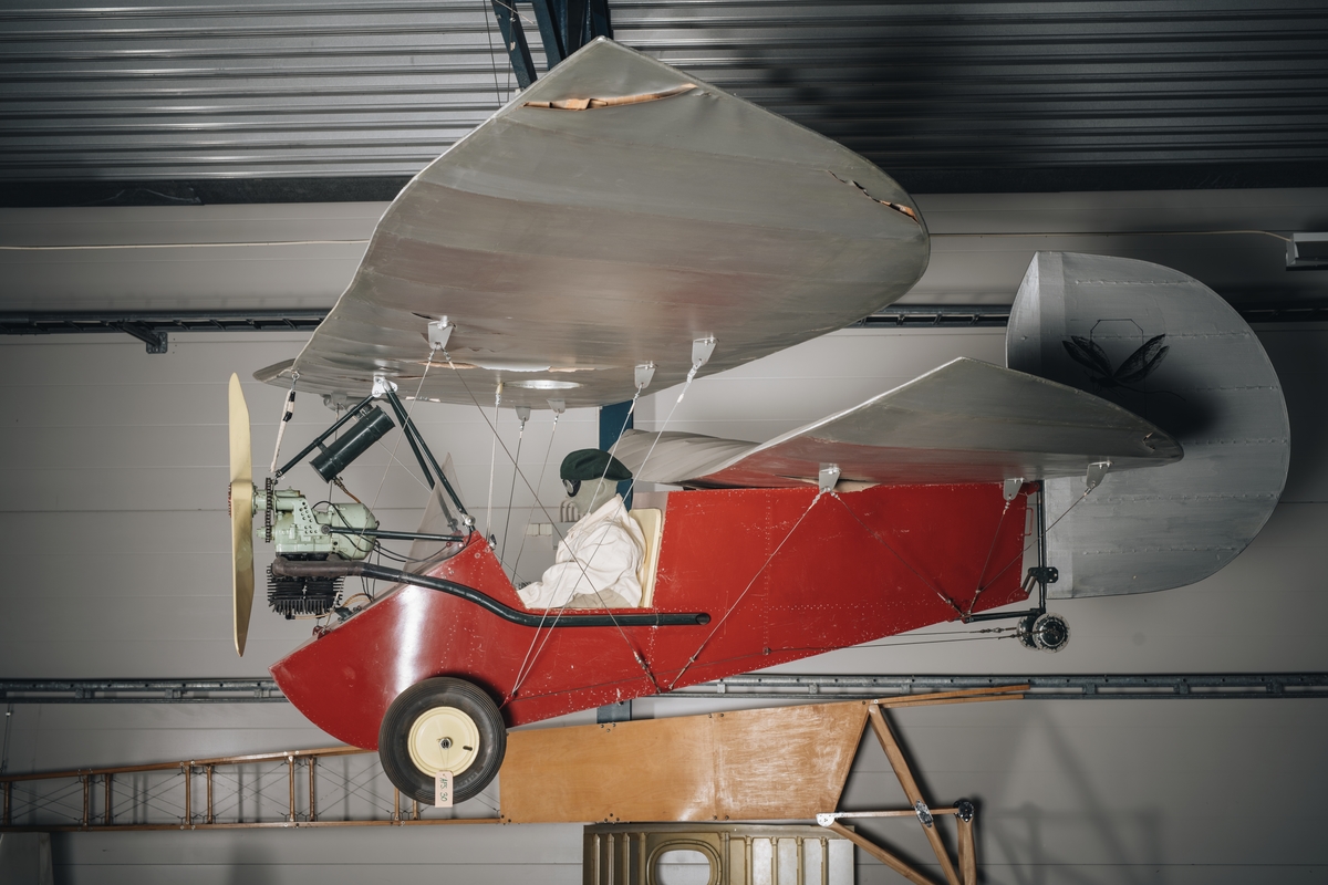 Flygplan kallat "Flygande loppan". Ensitsigt hembyggt propellerflygplan. Motor av märket DKW. Rödmålad flygkropp och silverfärgade vingar. På båda sidor av sidrodret finns målning av en loppa.