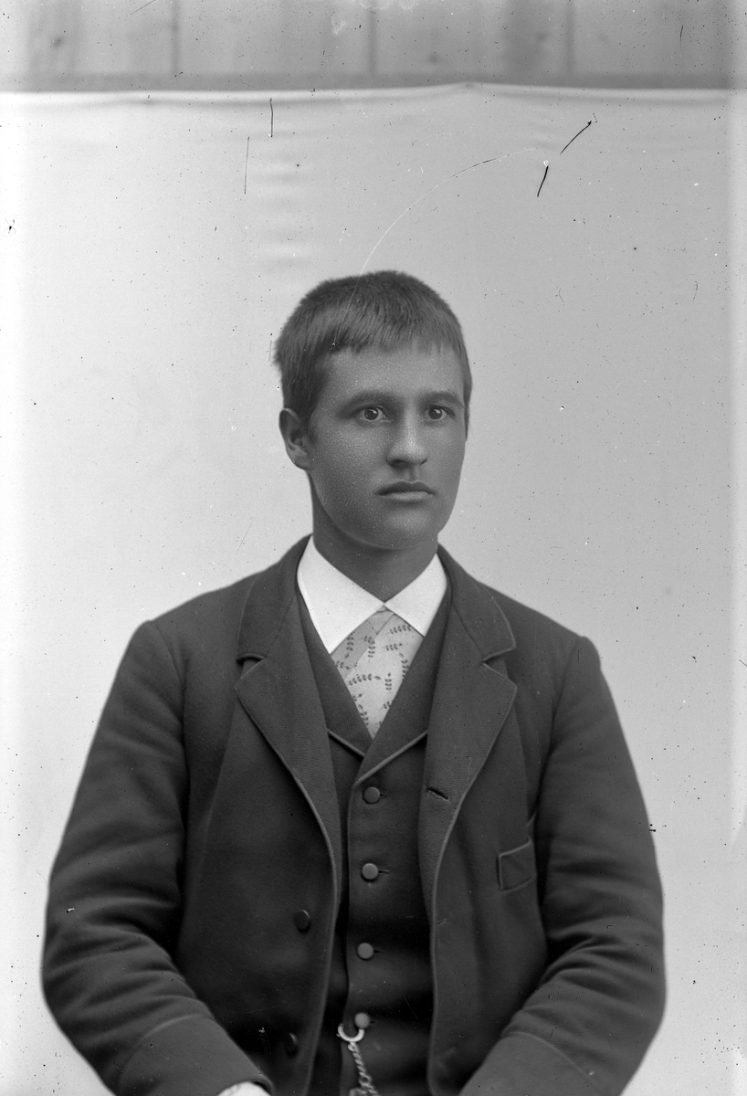 Ung mann i mørk dress og mønstret skjorte.