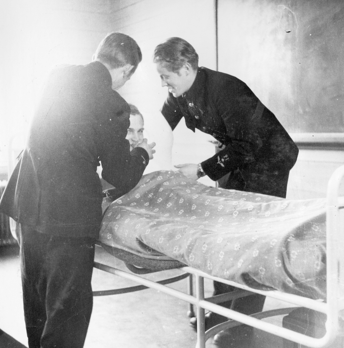 Två soldater ger en man i en sjuksäng något att dricka under sjukvårdskurs på F 11 Södermanlands flygflottilj, 1945.

Ur fotoalbum "Sjukvårdsskolan 15/1-15/3 1945" från F 11.