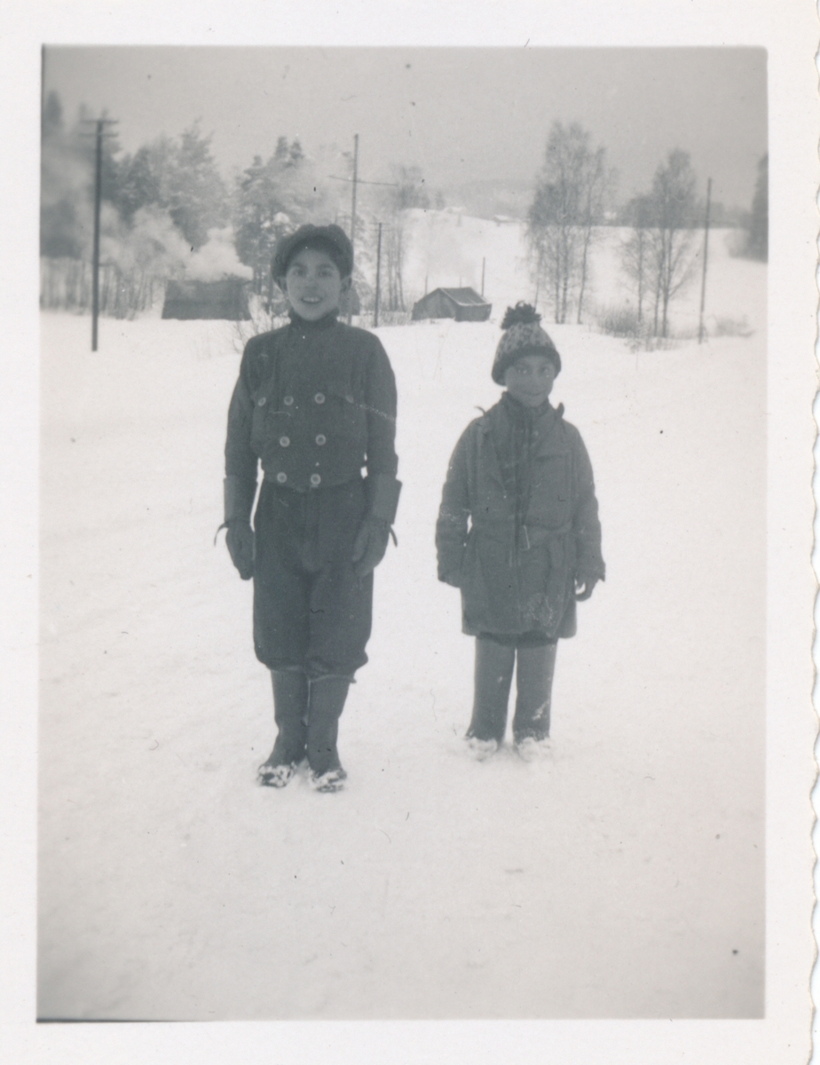 Två pojkar i ett snöigt landskap ler mot kameran. I bakgrunden skymtar tält.