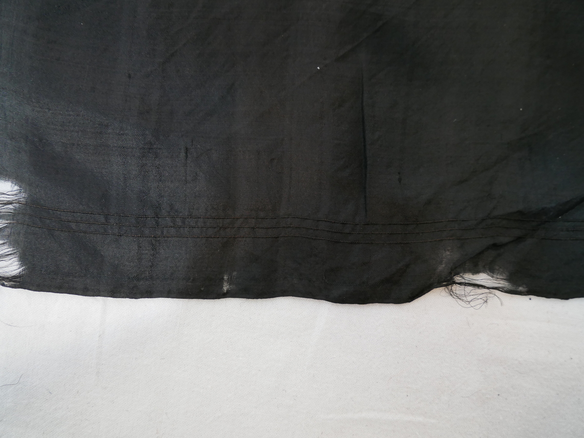 Tilnærmet kvadratisk silkeklut i svart. En bord med tre striper går rundt hele kluten. 