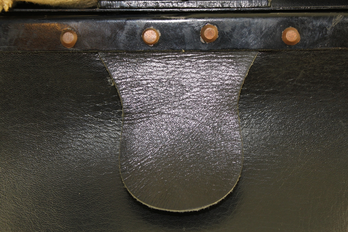 Brevbärarväska av svart läder med bygel, tillslutningsanordning och axelrem, 4 cm bred av naturfärgad väv. På framsidan ett påtryckt "silver" emblem och under bygelplösen en japansk inskription.

Ej använd.