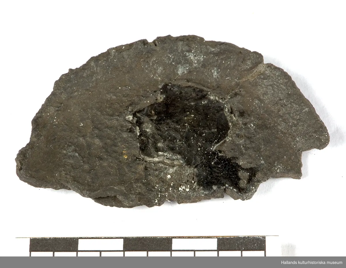Ett fragment från ett oidentiferat föremål i järn bestående av en halvcirkelformad platta i järn.