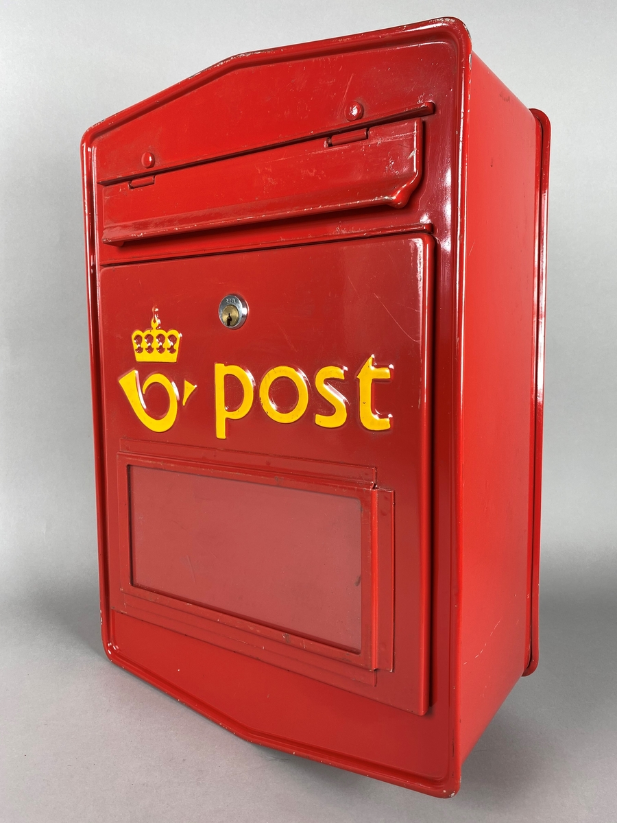 Rød postkasse med "vindu" for tømmeplakat. Med luke for innslipp av brev, og et låsbart lokk i front for tømming av post. Gul postlogo og skrift.