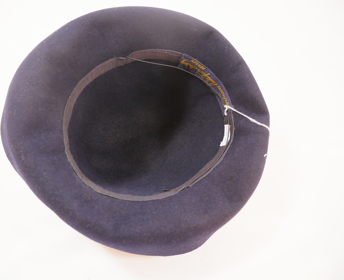 Form: Stor pull, avkorta for inni, bretta brem og svart silkeband rundt pullen. Har også ei lang hattenål med kvit "stein".
