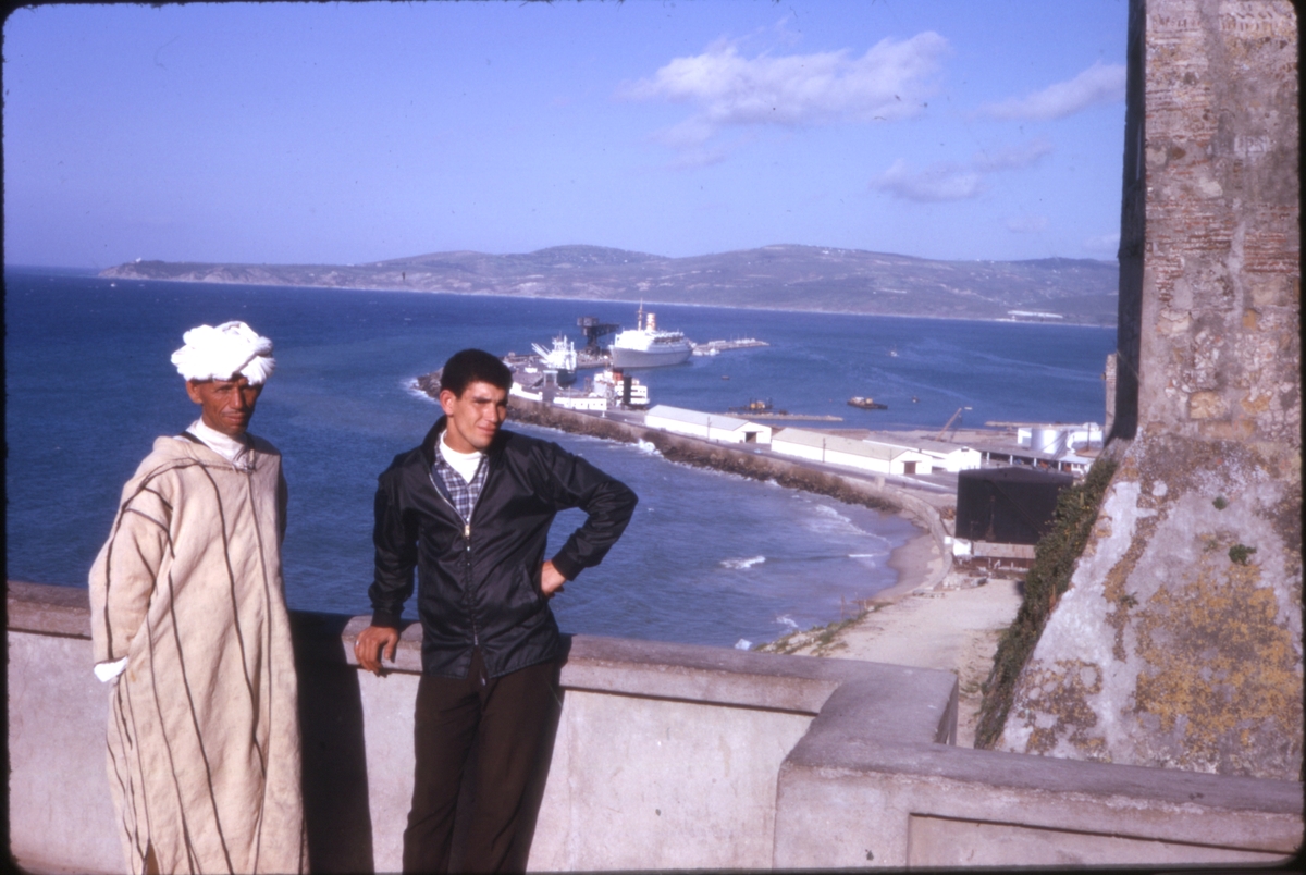 To menn ved kysten, med cruiseskipet 'M/S Sagafjord' i bakgrunnen, trolig i Tanger, Marokko. 'Sagafjord' Spring Cruise to Europe 1966.