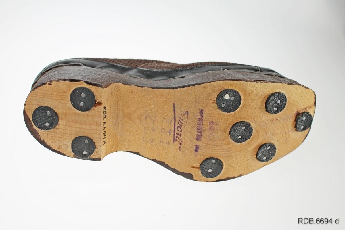 Et par brune barnesko. Skoene er "krigsvare", fra 2. verdenskrig, med overlær av strie og tresåler (trebunner). Foran på tåa, på hælen og rundt kanten på skoen er påsydd en forsterkning av svart kunstlær som er spikret fast til trebunnen. Foran på skoen er det åpning med tunge under og 3 par hull med maljer, med brune skolisser er tredd gjennom. Under sålen er fastspikret 9 gummiknotter, tre av dem på hælen. Skoene er ikke brukt.