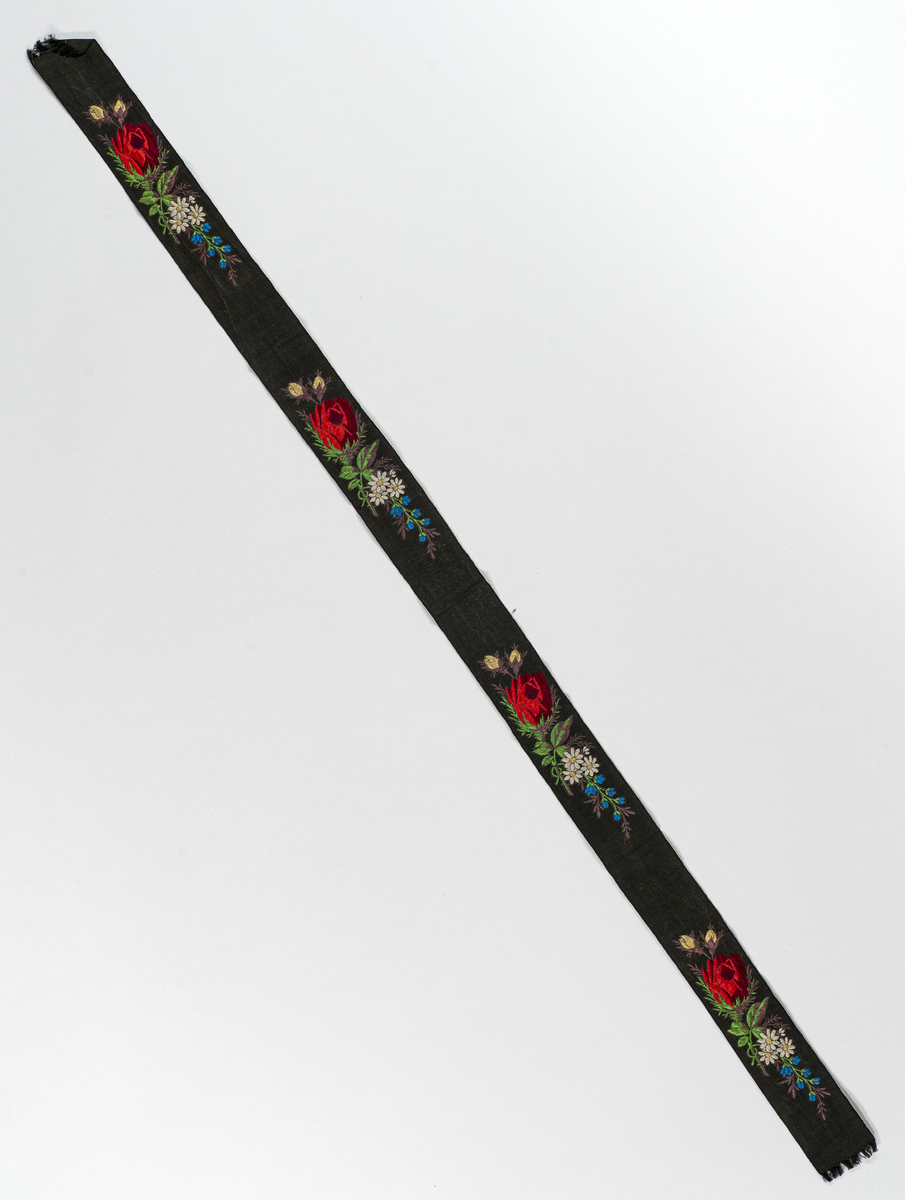 Sløyfebånd med påbrodert blomstermønster. Lå i liten, bordert veske (PEM.177) ved museets overtakelse. 
Har tilhørt Sara Fabricius.