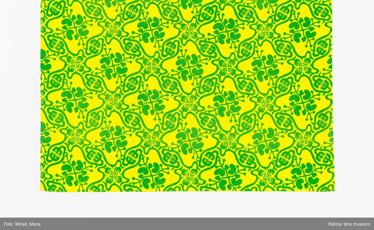 KLM 46157:683 Tyg. Metervara. Tryckt mönster på vit tuskaftad bomull.
Mönster med rombställda gröna växtslingor mot gul botten. Fållad för hand med tråckelstygn längs kortsidorna.