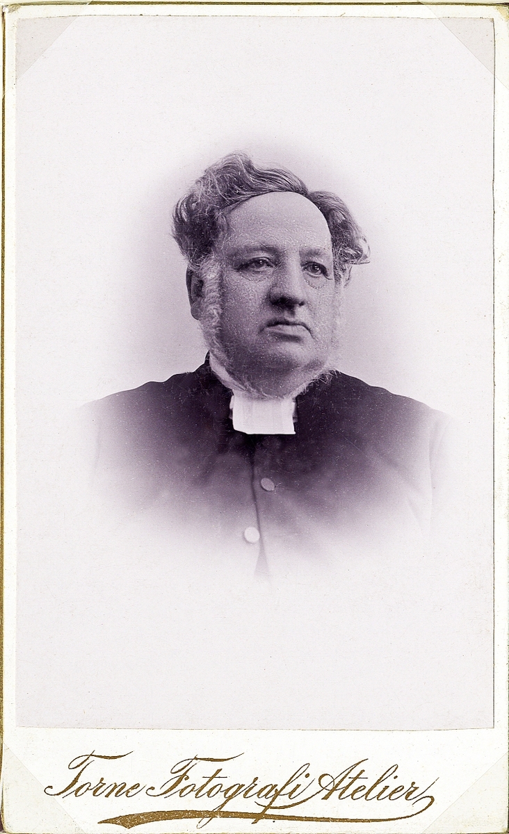 Porträttfoto av en man i prästdräkt m.m. 
Midjebild, halvprofil. Ateljéfoto.