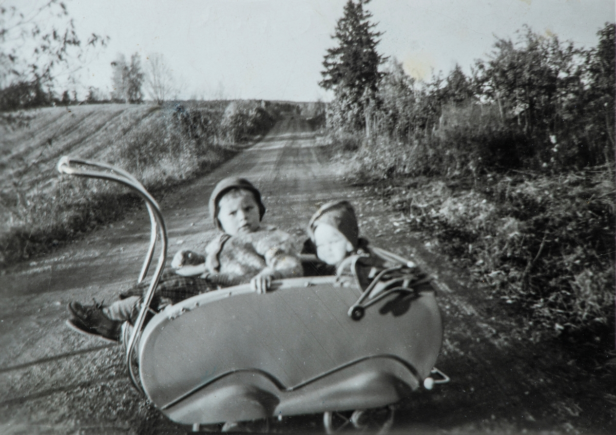 2 barn sittende i en barnevogn. I barnevogna Tove Pedersen og Grethe Pedersen, bildet er tatt på Grønlund, 84/7, på 1950 tallet.